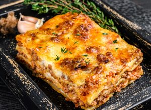 Portie lasagne met gehakt en tomaten bolognese-saus geserveerd in een houten schaal.